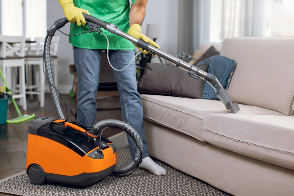 Close up of male janitor doing cleanup of couch with vacuum