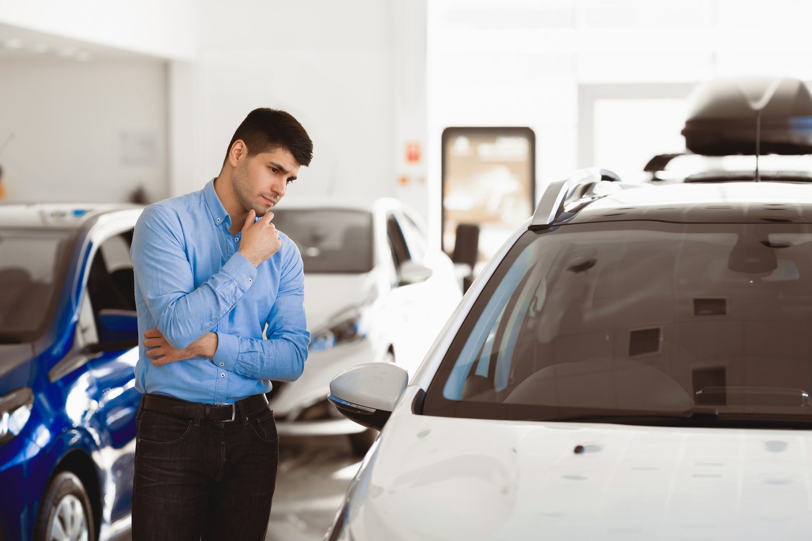 Man Looking At Auto Standing In Dealership Showroom